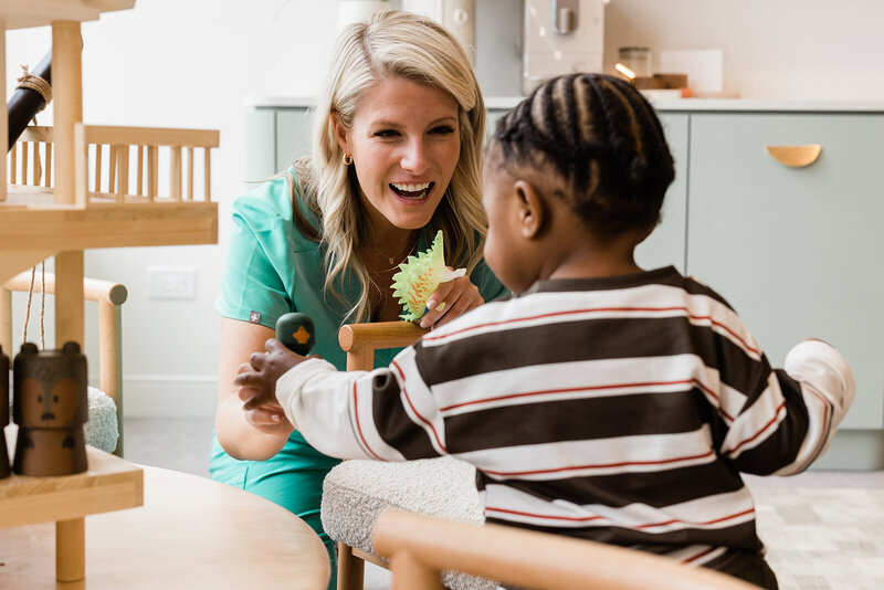 A smiling dental hygienist with pretty, curled blonde hair, chats with a young, multicultural patient in Chicago kids dentist office, Little Chompers.