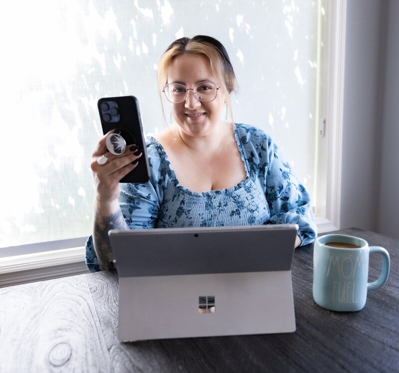 Woman works on her phone at a dining room table  with her tablet and a cup of coffee