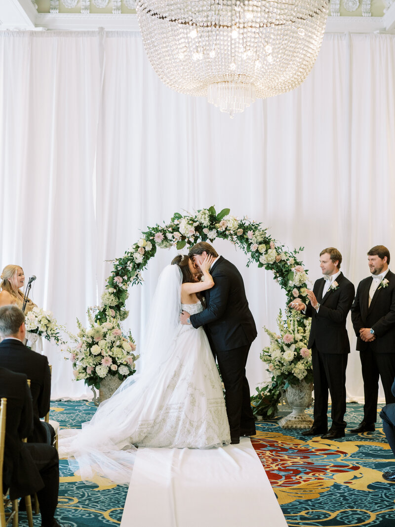 Black-tie wedding ceremony under a grand chandelier, documented by a Washington DC and Seattle-based luxury wedding photographer.