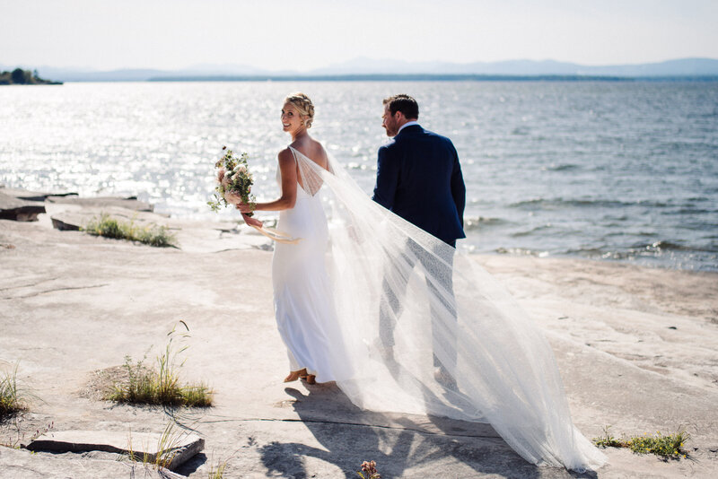 bride looks over her shoulder with shimmering lake behind her at vermont wedding