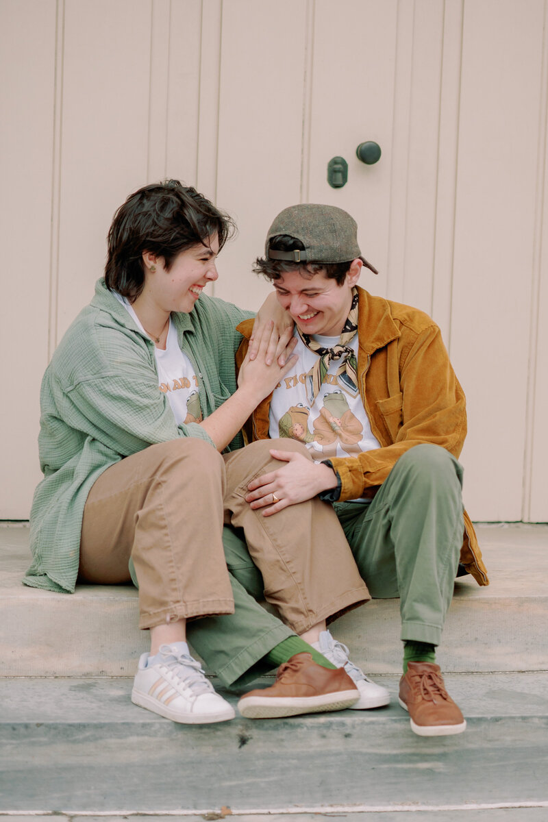 A couple poses outdoors, one wearing a backwards cap.
