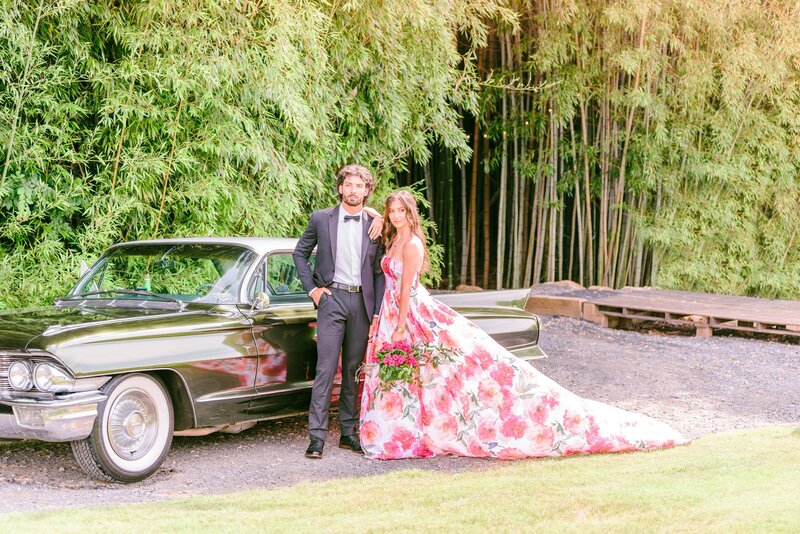 A groom and a bride in a pink dress stand with their car in front of the bamboo forest at Camelot Meadows.