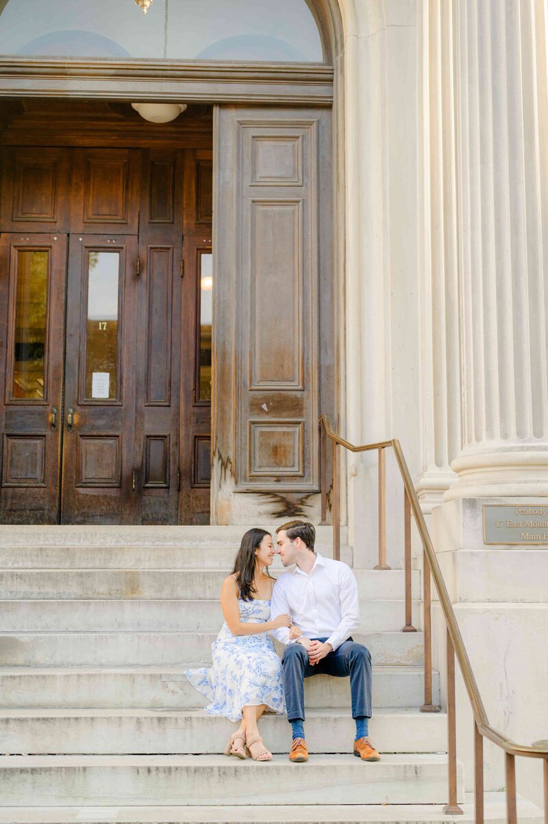 Bride and bridesmaids smile joyfully holding white parasols and fans. They are in front of a yellow building, conveying a lively, celebratory mood.