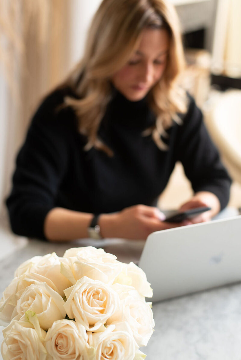 Laura Gatsos Young seated at an open macbook pro working on copywriting with cream roses in the foreground