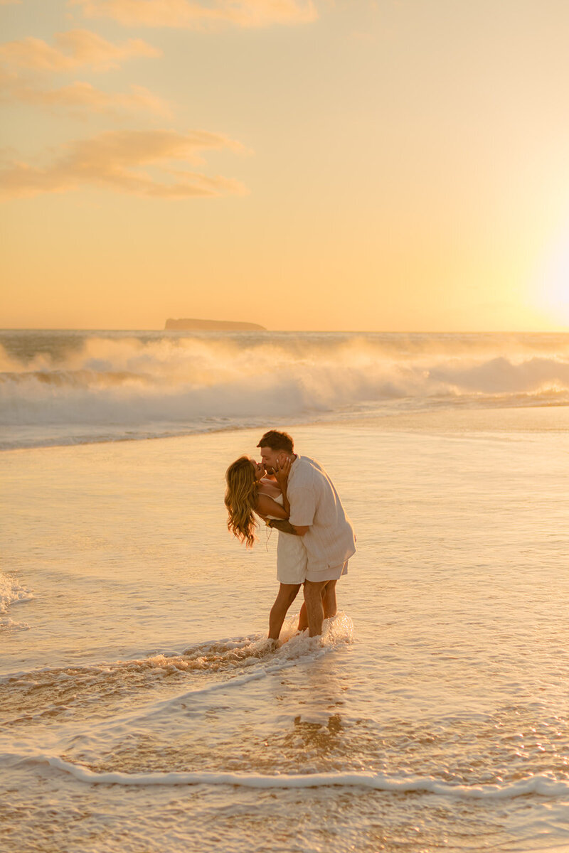 newly engaged couple kiss on the beach in hawaii during their engagement session with love and water photography