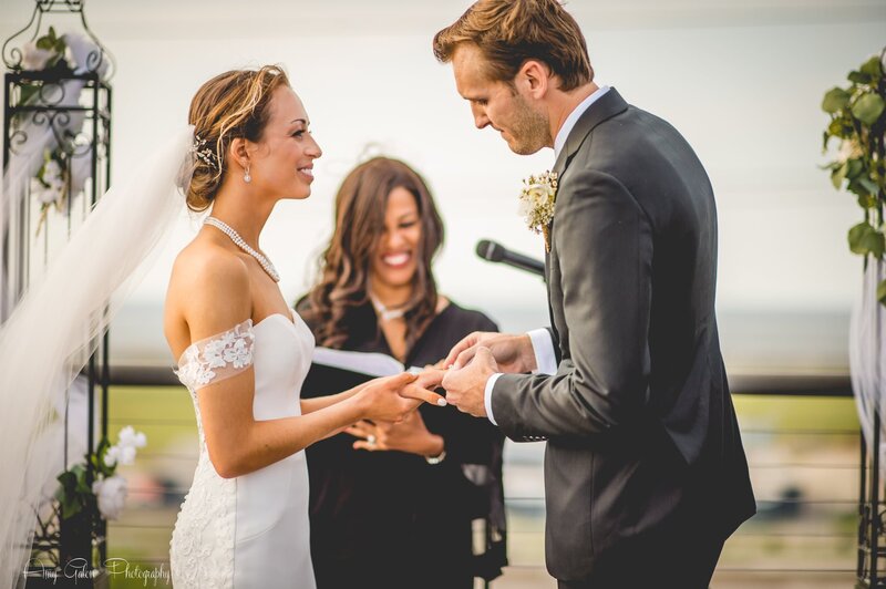 groom putting a ring on bride's hand with the officiant behind them
