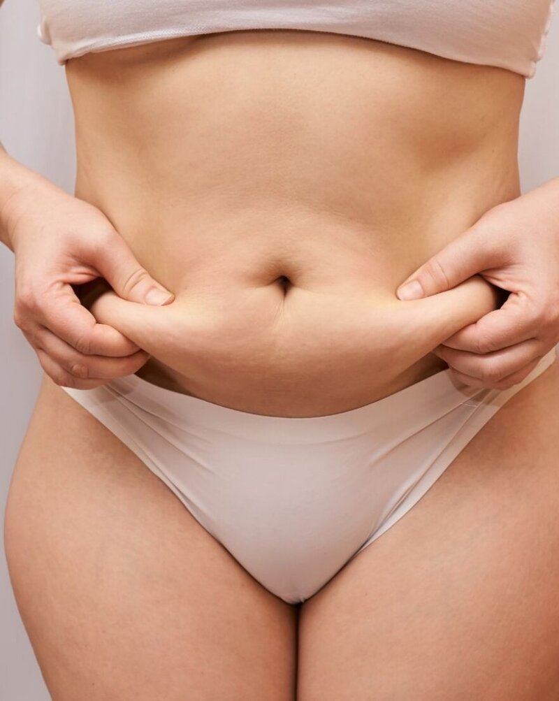 Focused close-up of a woman in white undergarments pinching her belly, highlighting the need for a targeted approach in Charlotte Hunter's Menopause Midsection Makeover program.