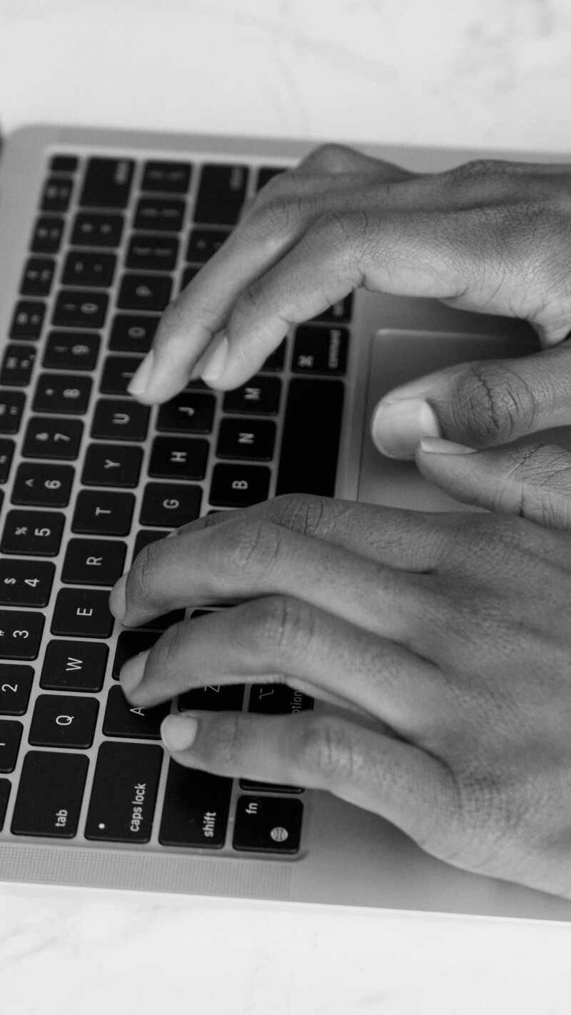 Black and white close-up of hands typing on a laptop keyboard