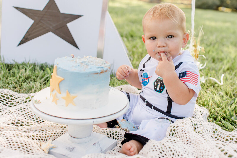 Baby boy licks icing off his finger during cake smash milestone session near Braselton, Georgia