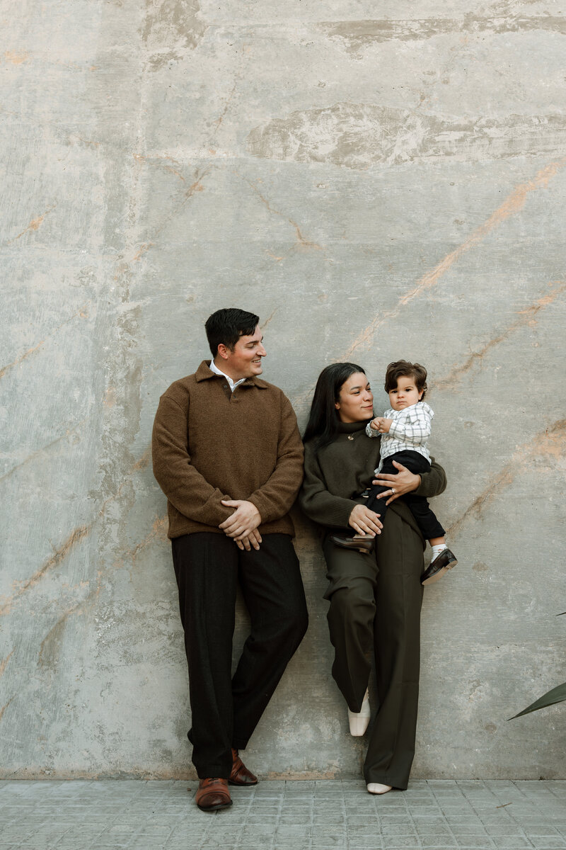 mom and dad holding toddler boy against a wall