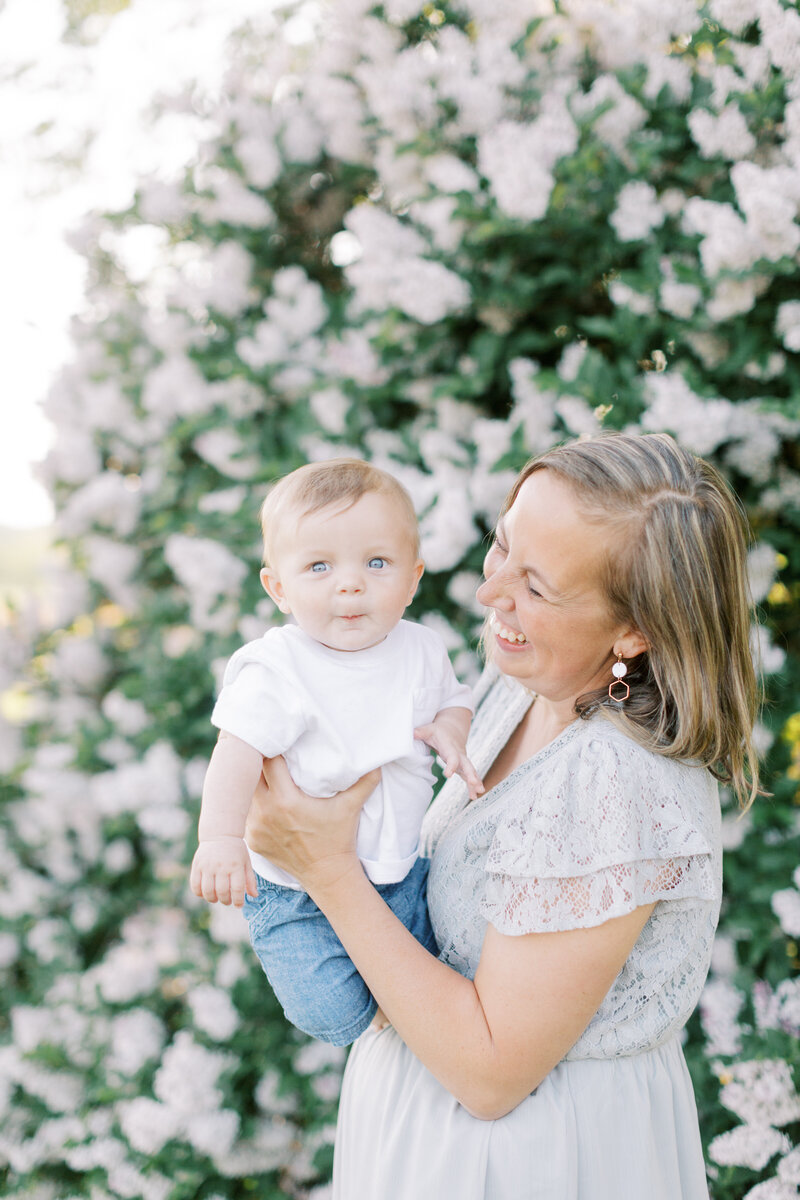 Mother holding baby in front of a blooming lilac bush