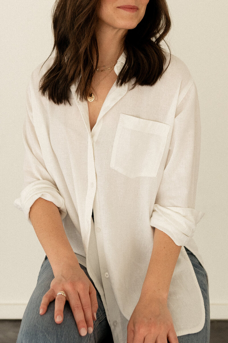 Close up of female SEO consultant wearing a white linen button down and dainty gold jewelry