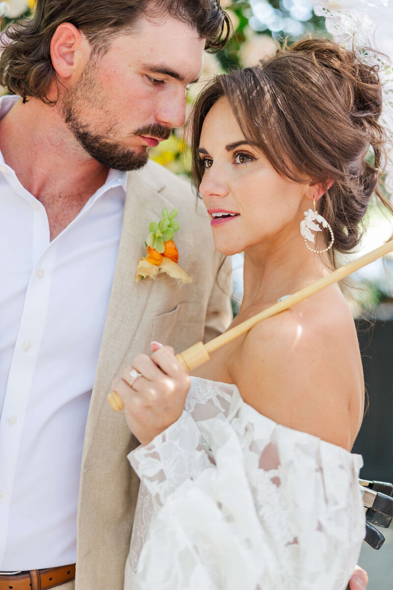bride stands in front of groom and takes her hand and places it on his cheek as he turns his face toward his smiling