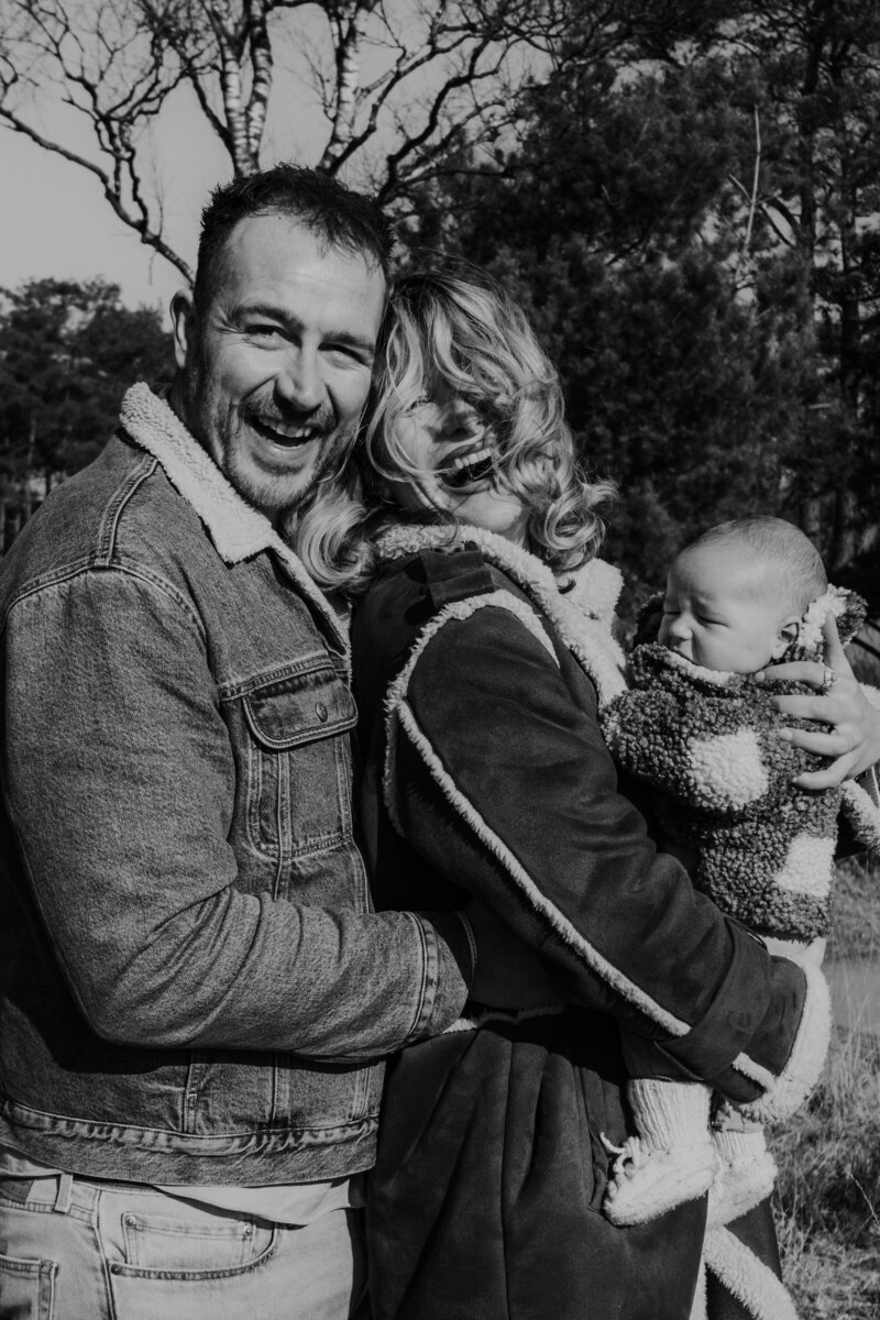 Een man en vrouw houden een baby vast in een uitgestrekt veld, omringd door natuur en zonlicht.