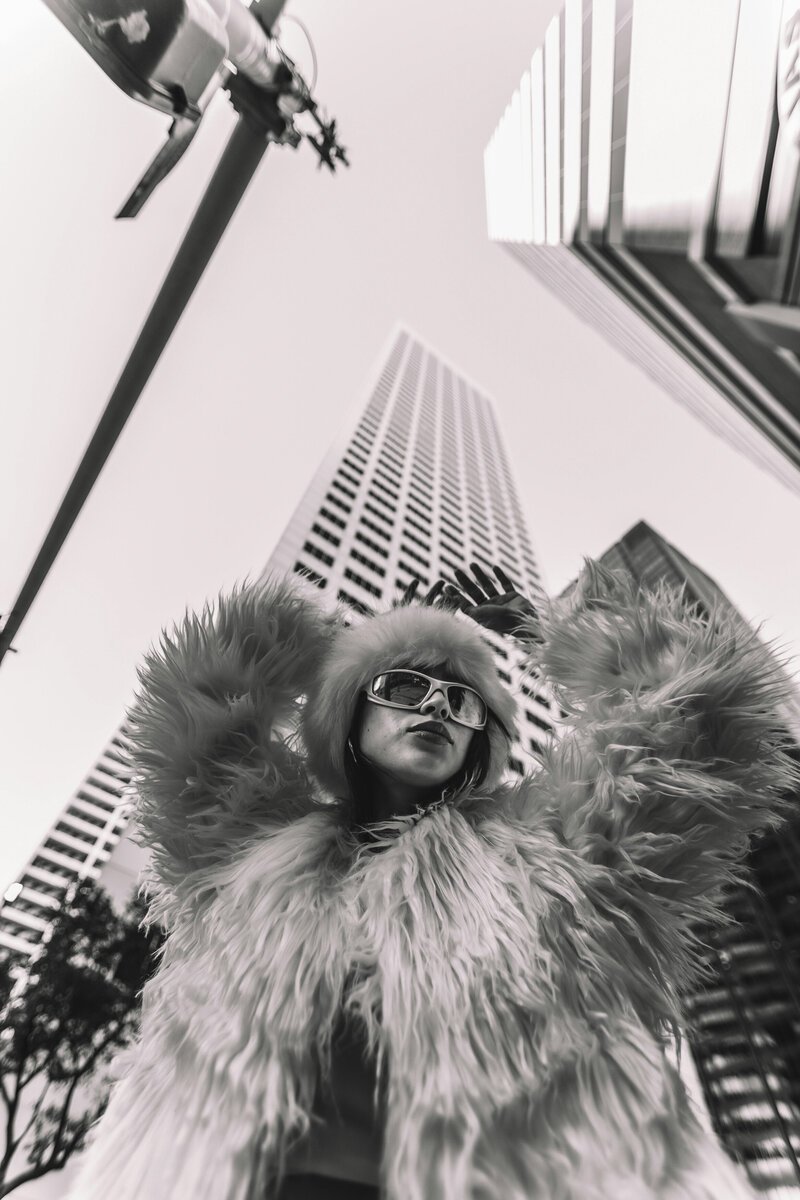 Bold black and white image of a woman in the city with sunglasses, a fur jacket, and fur hat, looking fierce. No more blending in! A strategic design showcases your personality, making you memorable in a sea of competitors.