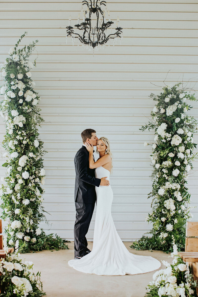 bride and groom standing between white floral displays