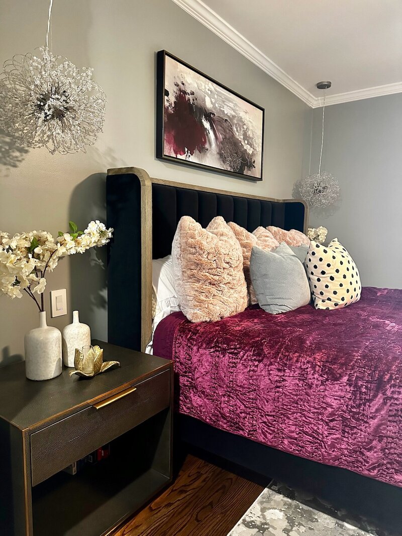 Bed with purple velvety sheets and textured pillows next to a night stand
