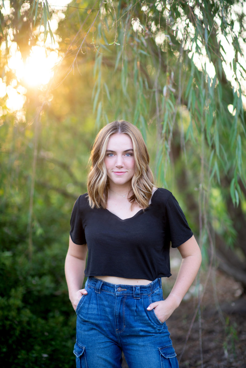 High school senior takes portrait outdoors under tree in black shirt