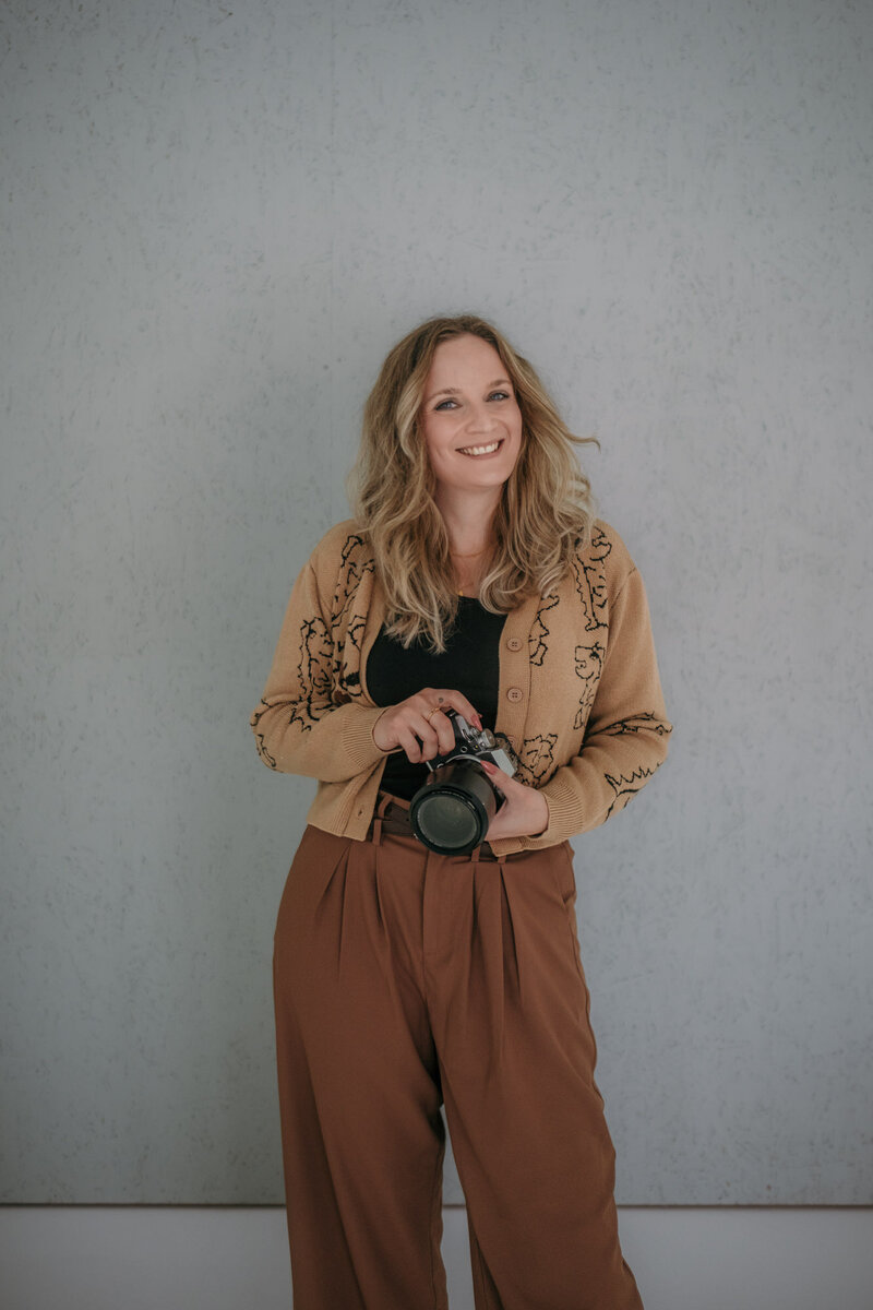Photographer Karin holds her camera while smiling.