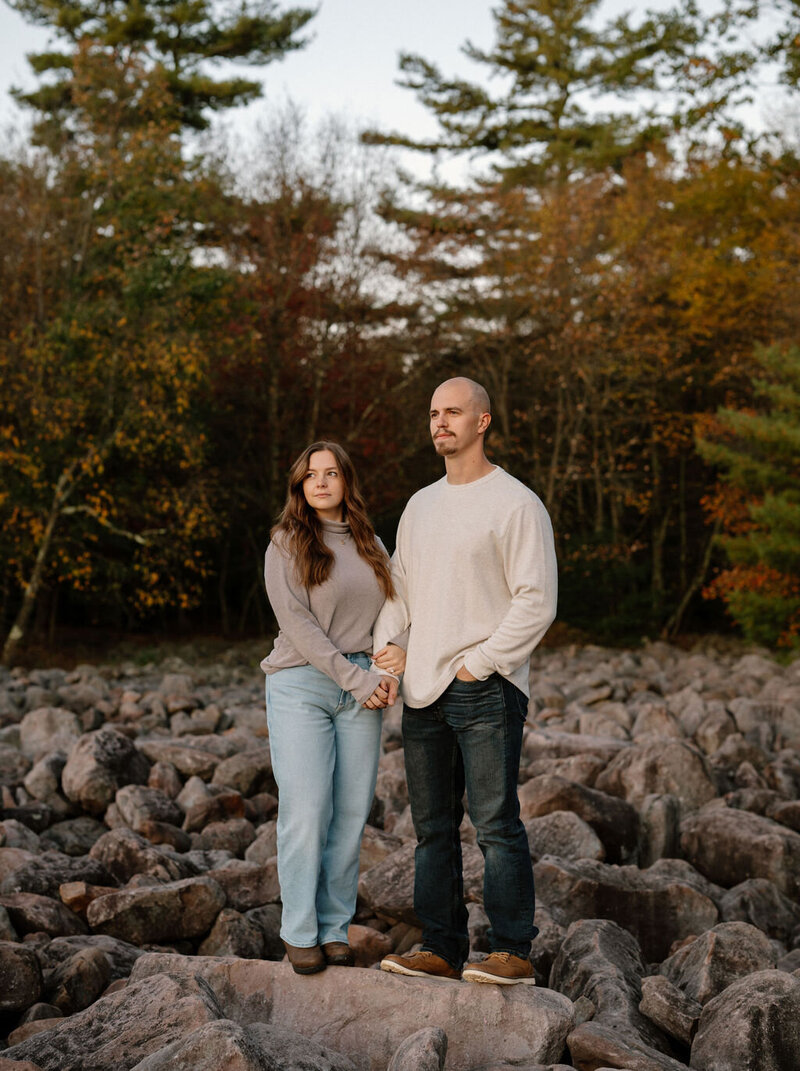 Engaged couple standing on rocks surrounded by autumn foliage during a fall session in New York, captured by NYC wedding and elopement photographer Dom Augustine.