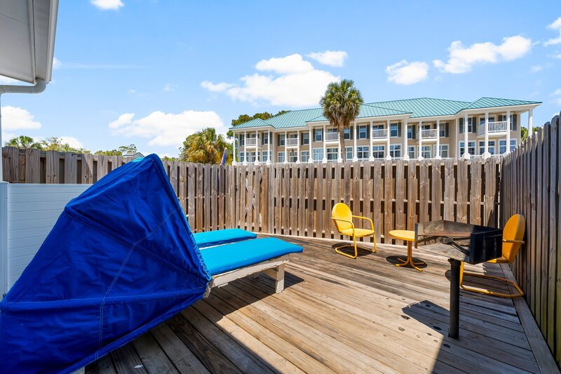 Fenced-in private patio with yellow vintage chairs, BBQ grill, and double loungers at Groovy Shack, minutes from the beach and near Grayton Beach and Destin.