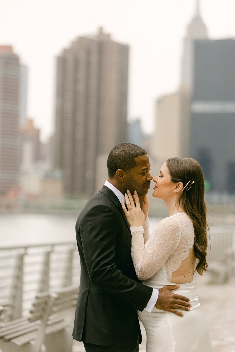A bride and groom stop to take a wedding photo with the New York City skyline in the background.