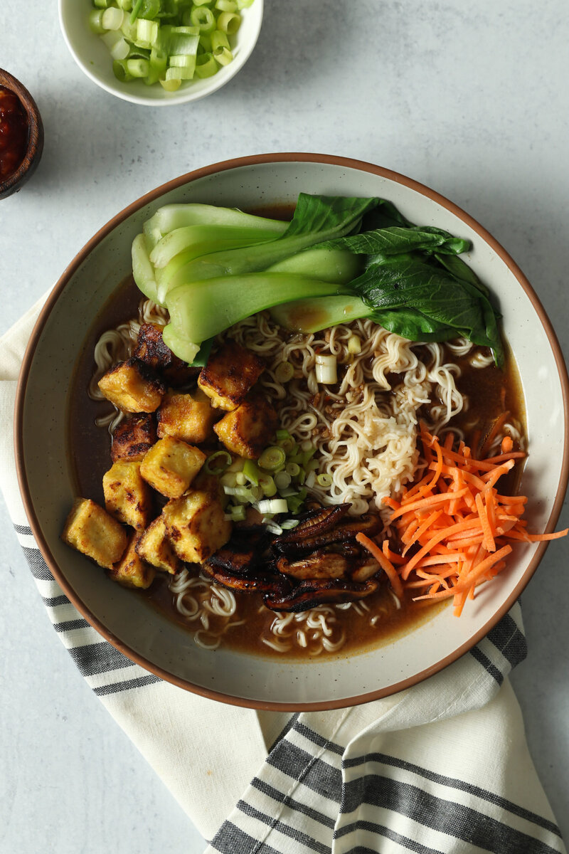 a soup with ramen noodles, tofu, carrots, and other vegetables