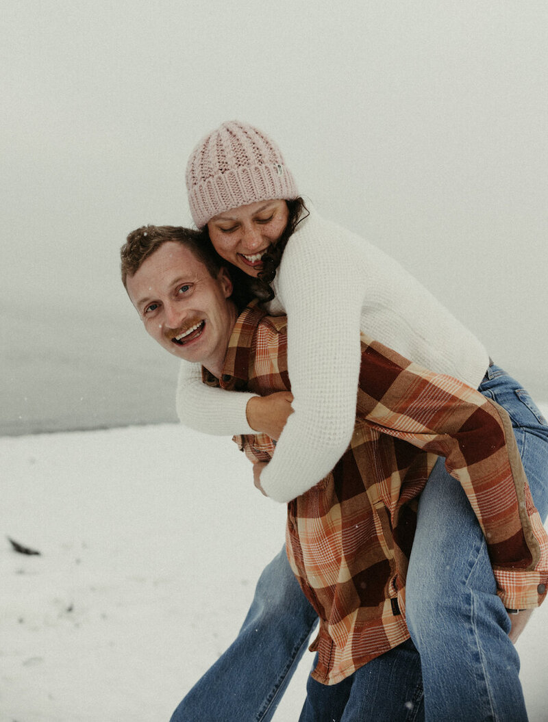 man giving woman a piggy back ride along the beach