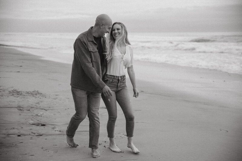 couple walks along beach for engagement photos in san diego