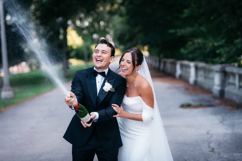 A groom playfully sprays champagne while the bride laughs joyfully beside him during their Four Seasons Chicago wedding, planned by Savoir Fête.