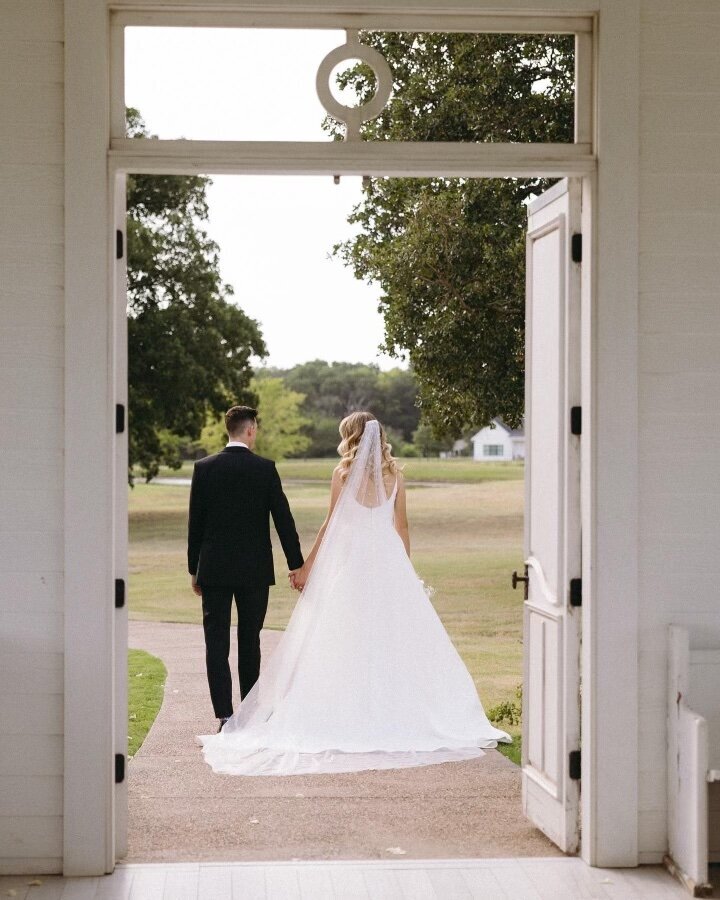 Bride and groom walking hand-in-hand through chapel doorway toward open field – romantic wedding photography by Madison Dodd Photo in Oklahoma