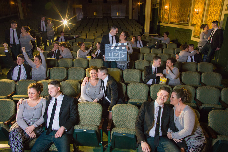 A playful engagement session inside a movie theater, featuring a couple sharing laughs and doing quirky poses among the seats and screens, blending fun and romance.