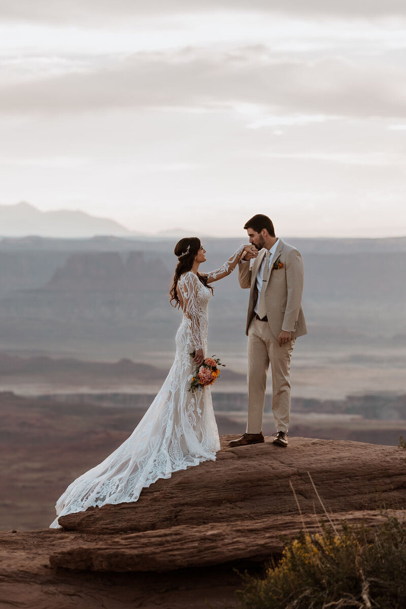 groom kissing bride's hand while standing in the desert