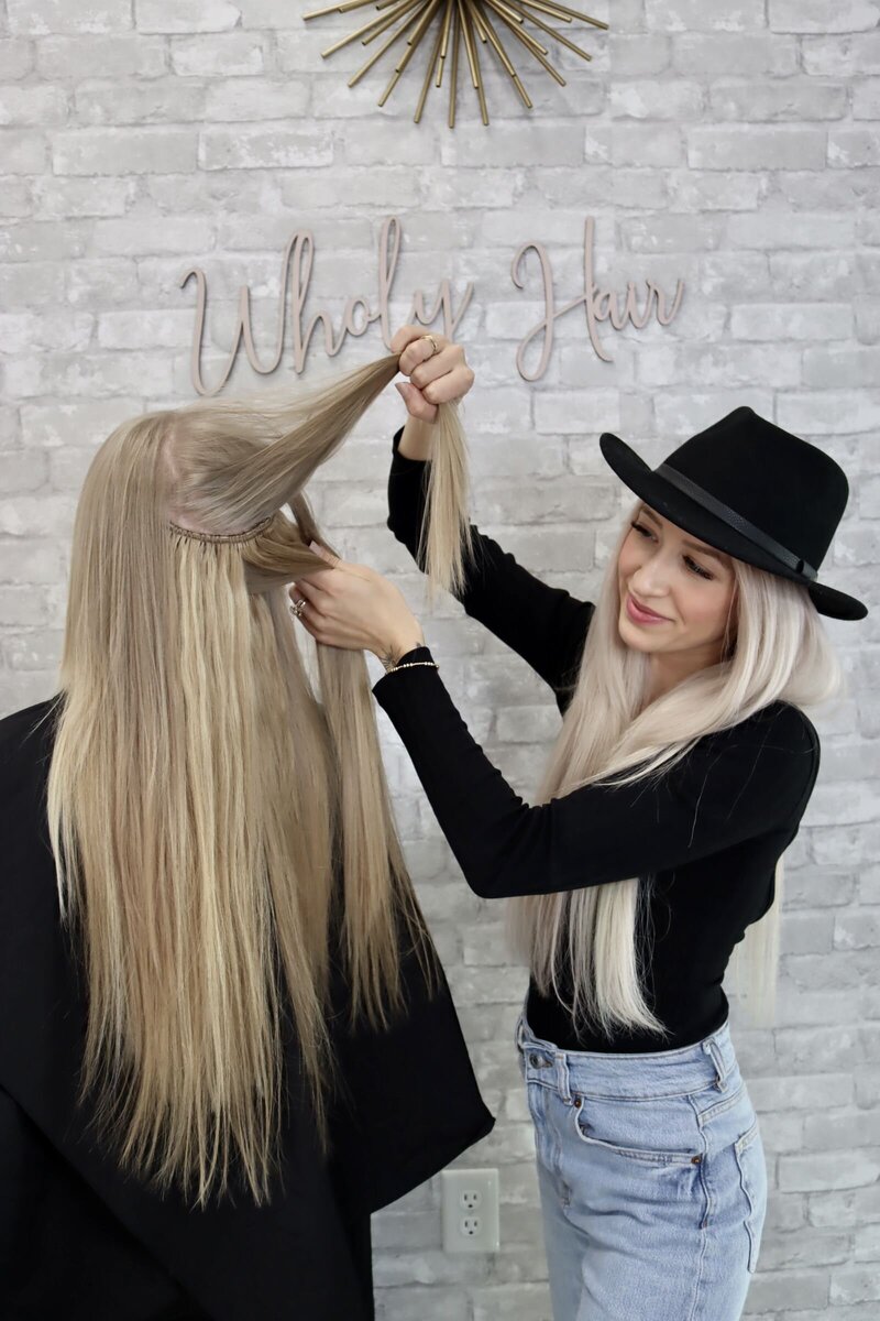 woman holding up her client's hair and showing her invisible beaded row hair extensions for virtual certification course