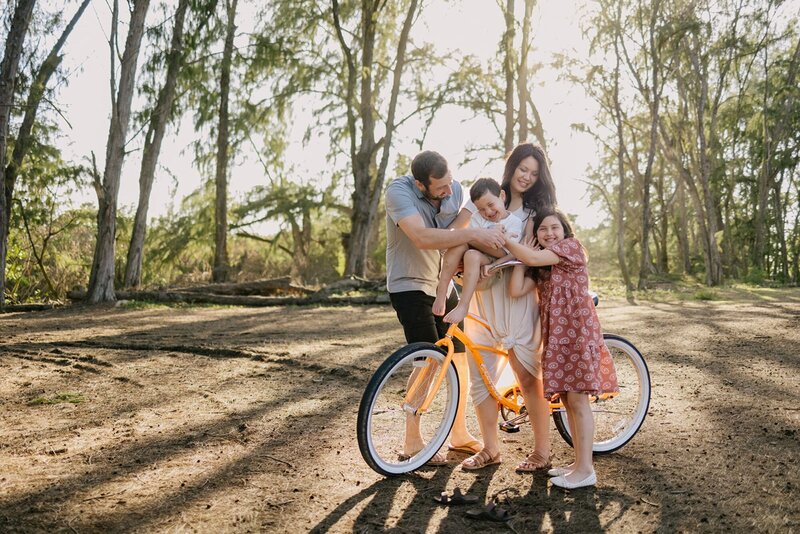 A family of four embrace, and hold each other next to their beach cruiser.
