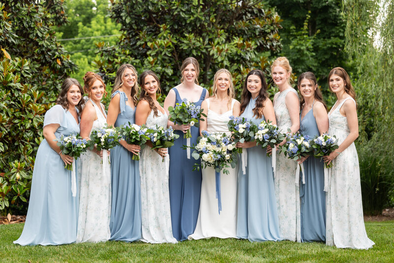 Spring wedding at WinMock at Kinderton, designed by Charming Carolina — bride and bridesmaids posing with dusty blue and greenery bouquets outside the venue’s barn.