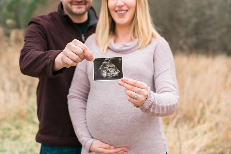 parents-to-be proudly holding an ultrasound of their baby while mom holds her pregnant belly