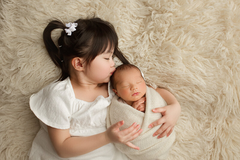 Big sister holding new baby brother all wrapped up on a rug