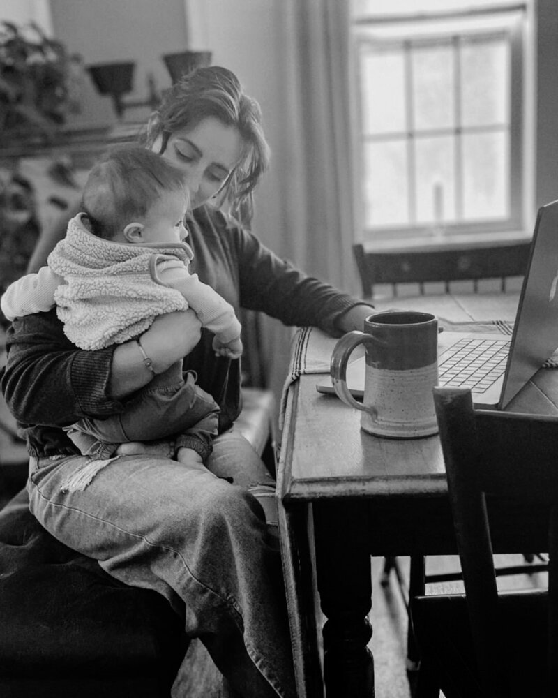 Web designer working on laptop from home, with baby on her lap