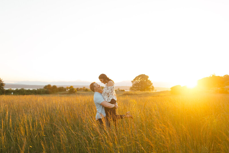 Engaged couple in the grassy knoll of Discovery Park in Seattle at sunset.