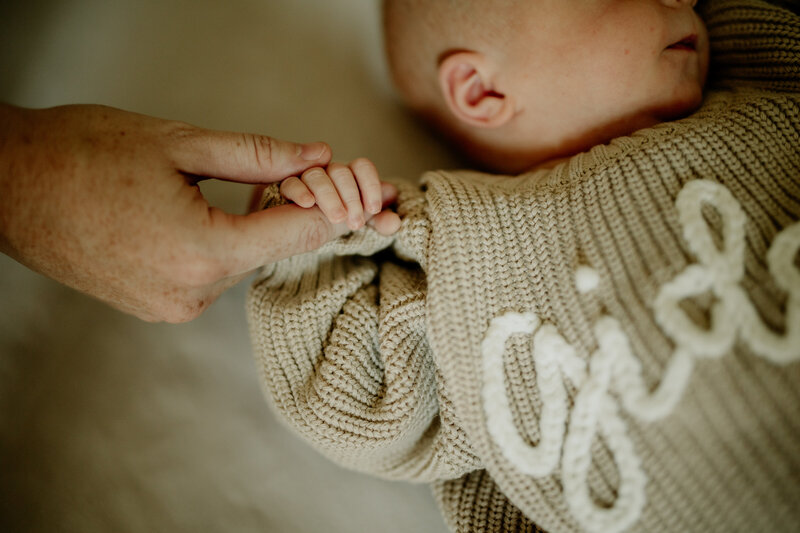 A tiny newborn baby wraps his hand around his dad's finger during an in-home newborn lifestyle session.