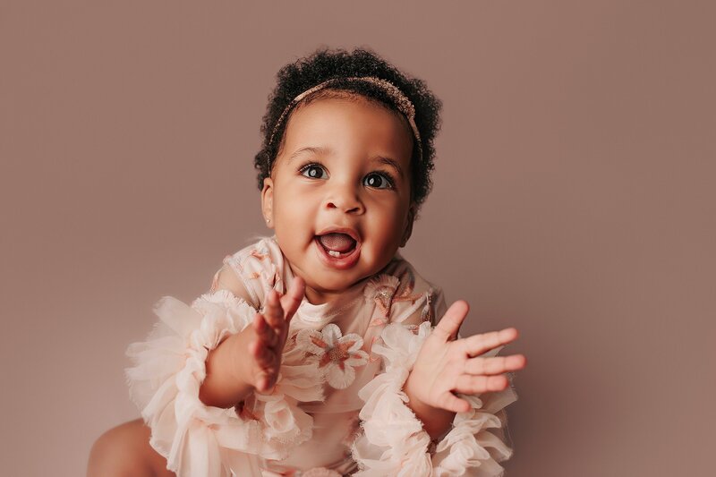  One-year-old baby laughing during fun, natural milestone shoot in studio