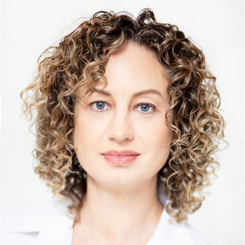 A headshot of Danielle Restivo in a white shirt with curly hair