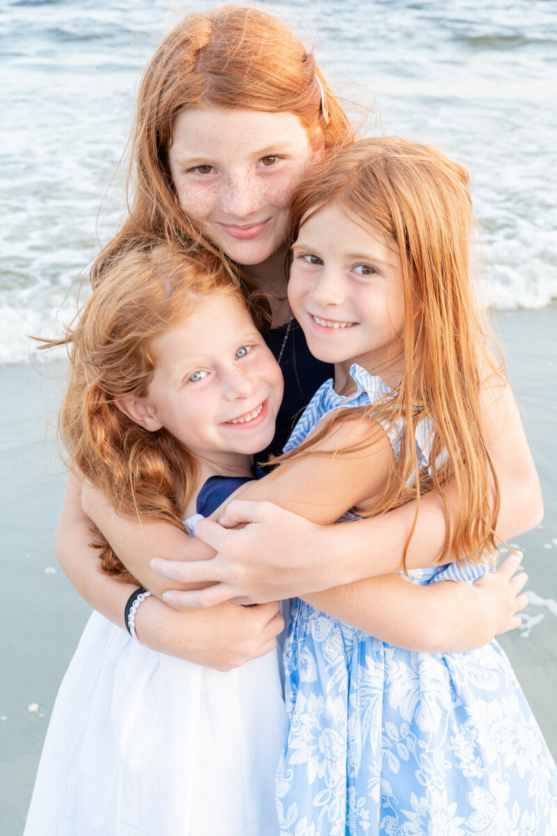 Three little red head sisters hug each other while looking at the camera