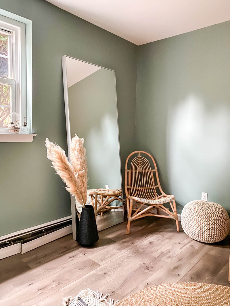 calming wall color with large mirror a stool and comfortable chair with pampas grass in vase
