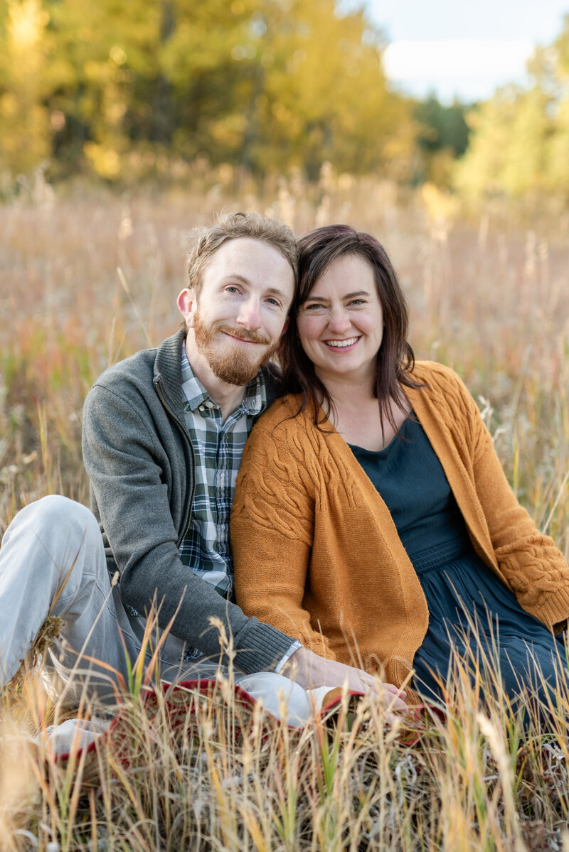 A couple seated in a field look at the camera, smiling