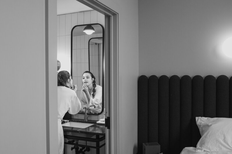 Woman putting on lipstick in the mirror in hotel room