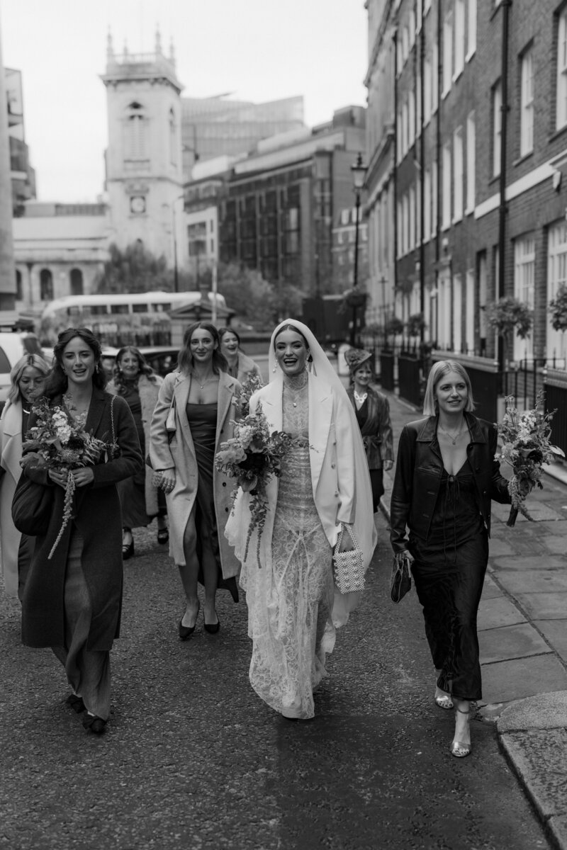 Bride walks hand in hand with here bridesmaids to her London wedding venue st etheldreda's church to get married.
