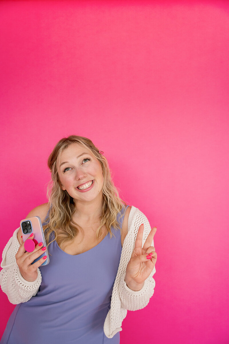 Kat Murphy taking a selfie in a light pink blazer putting on orange flower sunglasses