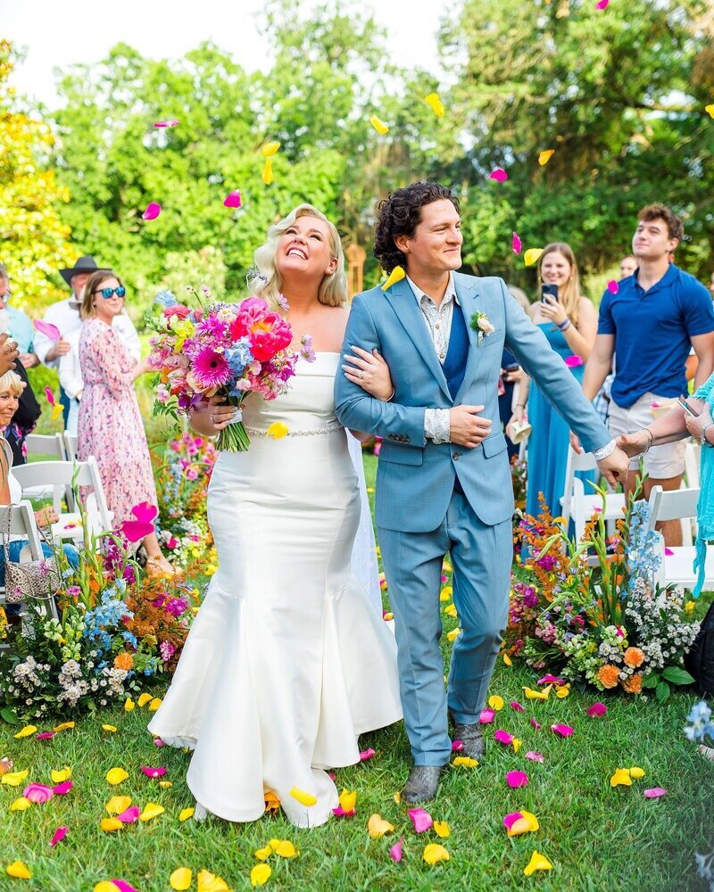 Newlyweds walking up the aisle with a colorful bouquet designed by Austin wedding florist Flora Fetish.